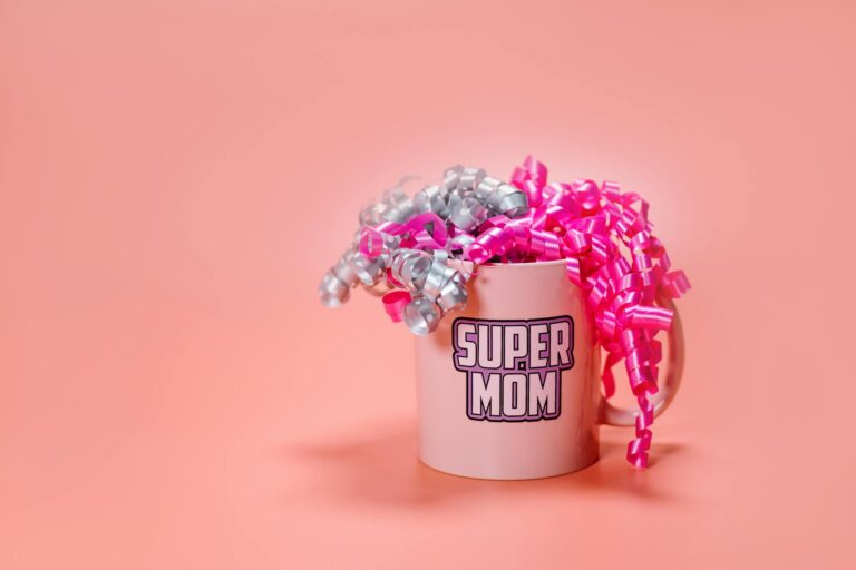 A festive 'Super Mom' mug wrapped with pink and silver ribbons against a pink backdrop. Perfect gift for Mother's Day.