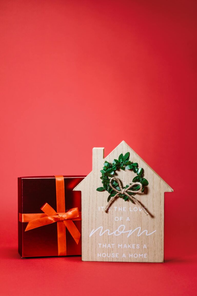 Wooden house sign and gift box on red background, perfect for Mother's Day gifting.