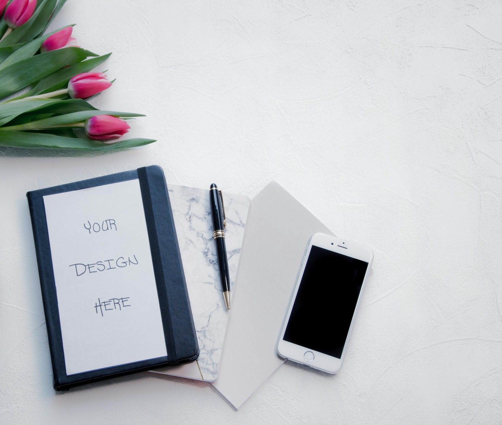 Flat lay of a workspace with tulips, a notebook, pen, and smartphone, perfect for designs.
